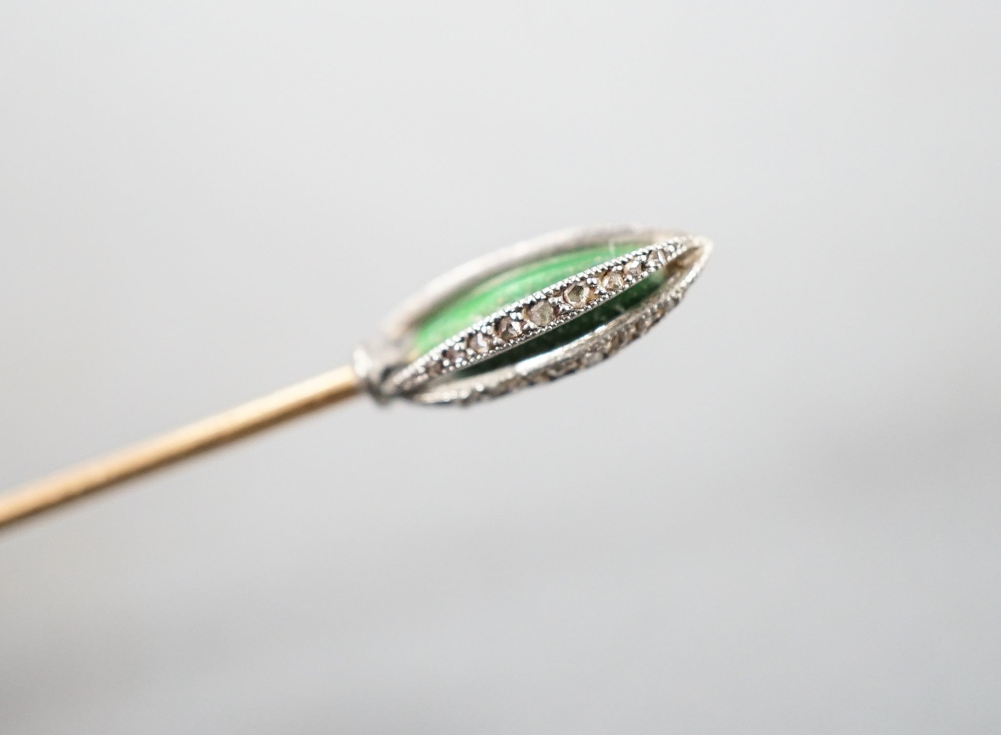 An early 20th century yellow metal stick pin, with rose cut diamond and green enamel set terminal, 76mm, gross weight 2.3 grams.